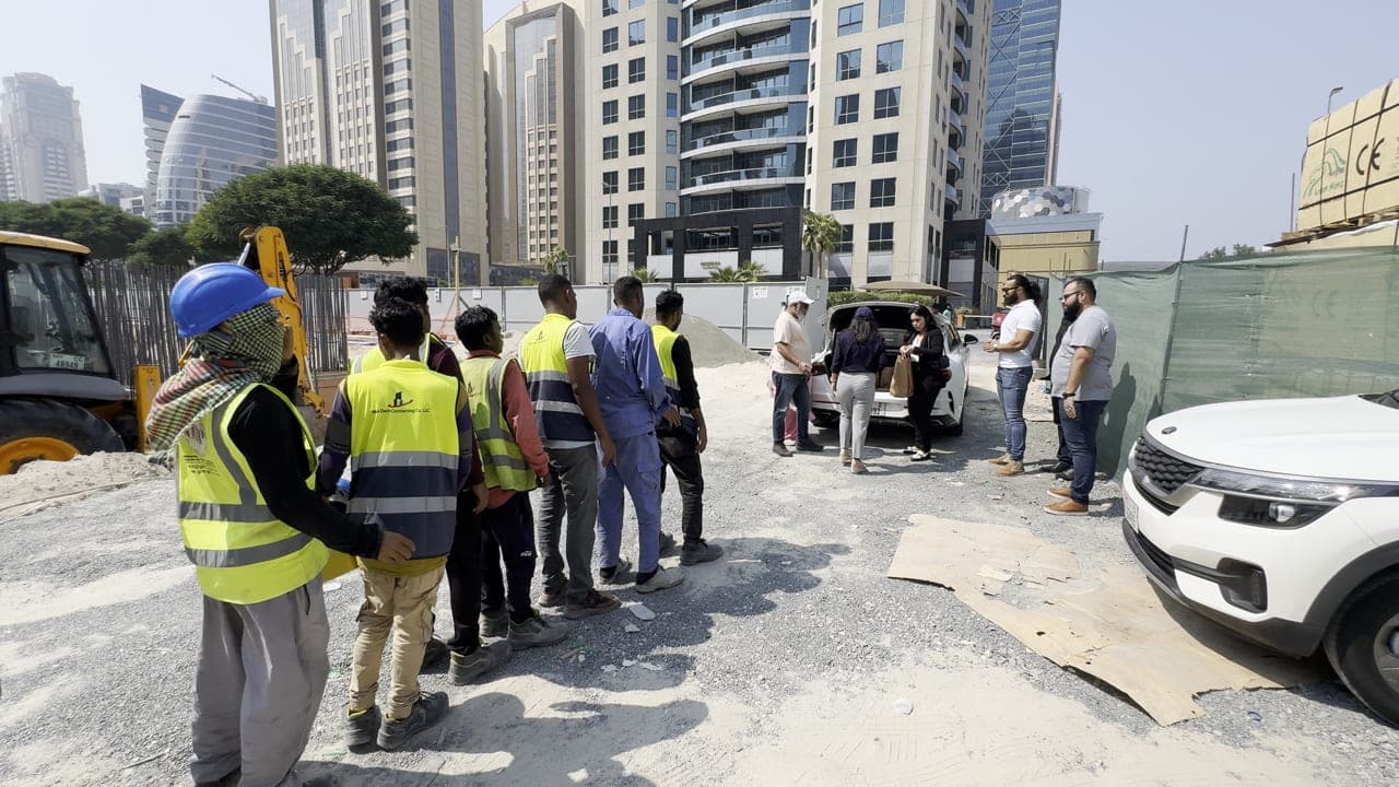 Construction workers in hi-vis vests lining up to receive packed meals in Dubai