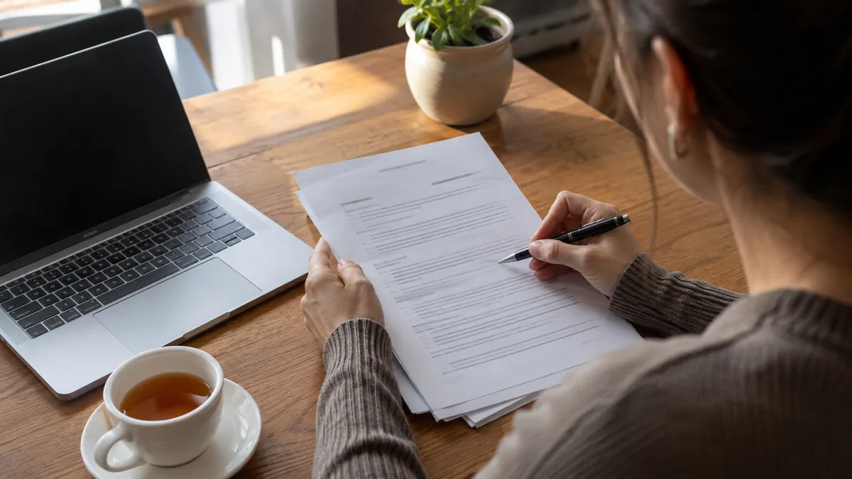 A tenant carefully reading the fine print of a tenancy contract at a table, pen in hand, with a laptop and tea nearby